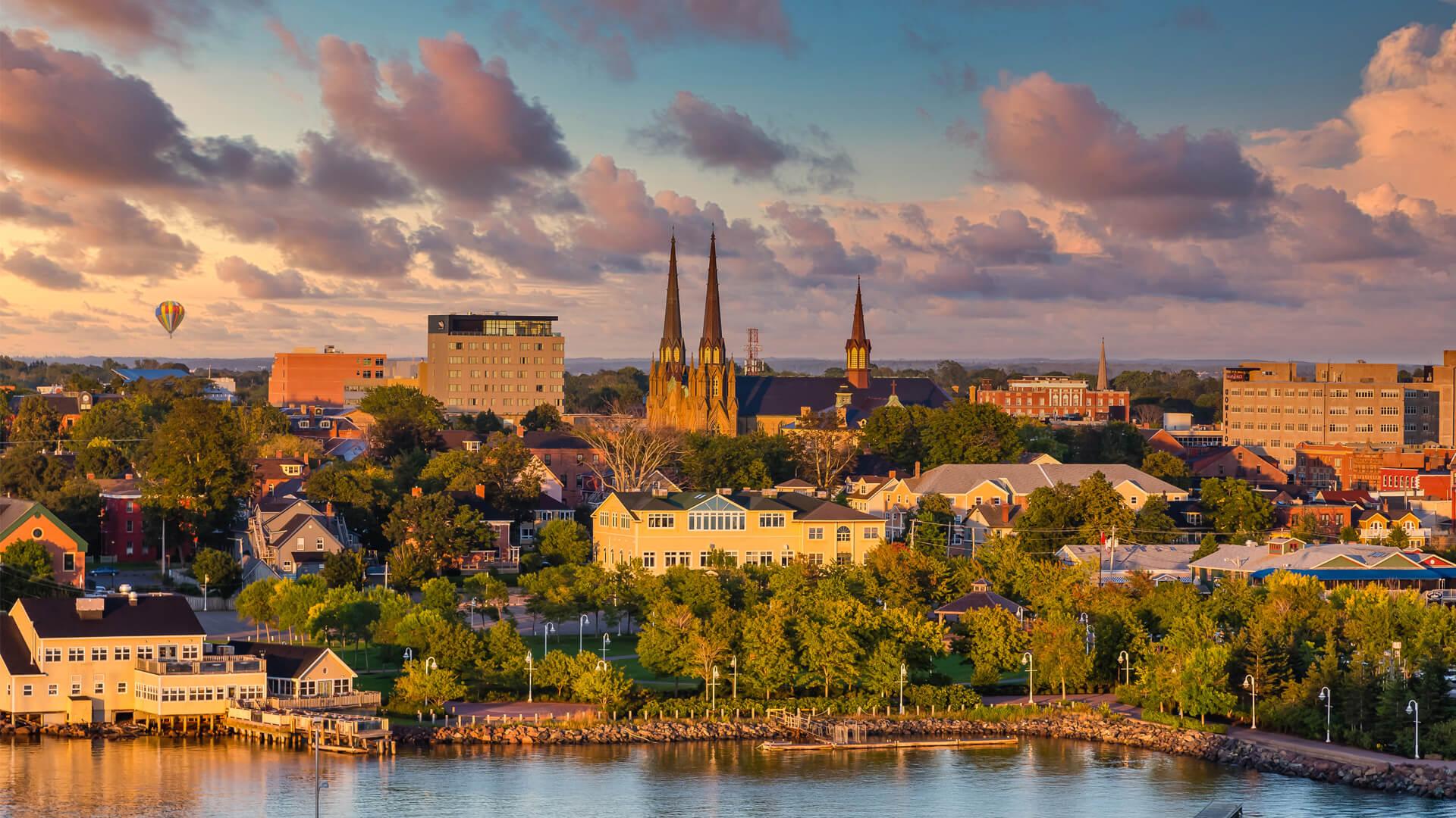 Panoramic view of Charlottetown featuring St. Dunstan’s Basilica, the waterfront, and a hot air balloon at sunset.