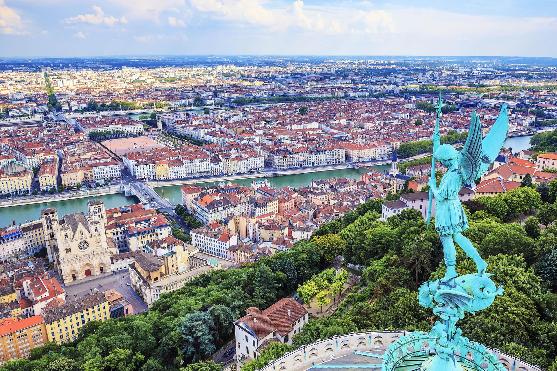 Panoramic view of Lyon with the Archangel Saint Michael statue rising above the city and the Saône flowing through it.