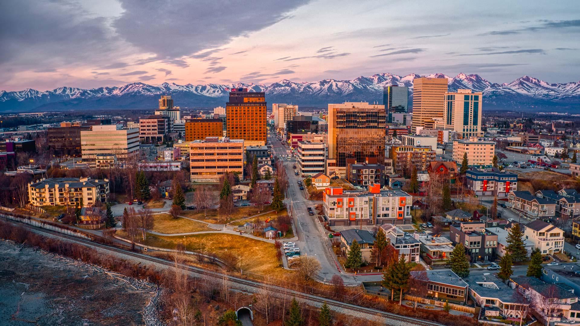 Vue aérienne de la ville d’Anchorage, en Alaska, avec ses bâtiments modernes et des montagnes enneigées en arrière-plan.