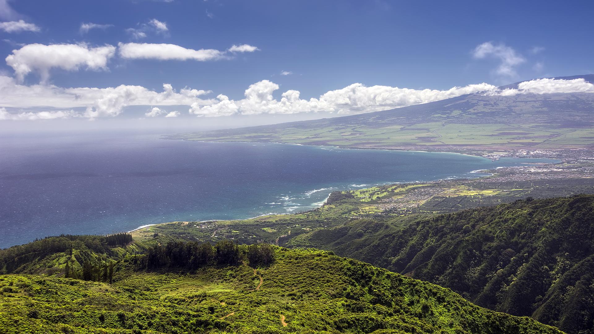 Aerial view of Kahului, Hawaii, with the Pacific Ocean, lush mountains, and broad slopes of Haleakalā in the background.