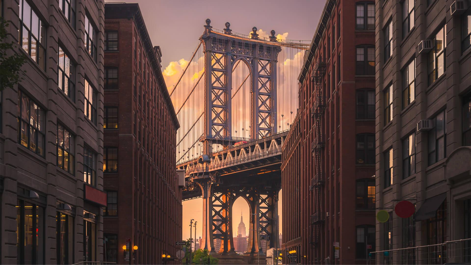 Pont de Manhattan vu depuis Brooklyn au coucher du soleil, avec l’Empire State Building encadré par l’arche du pont.