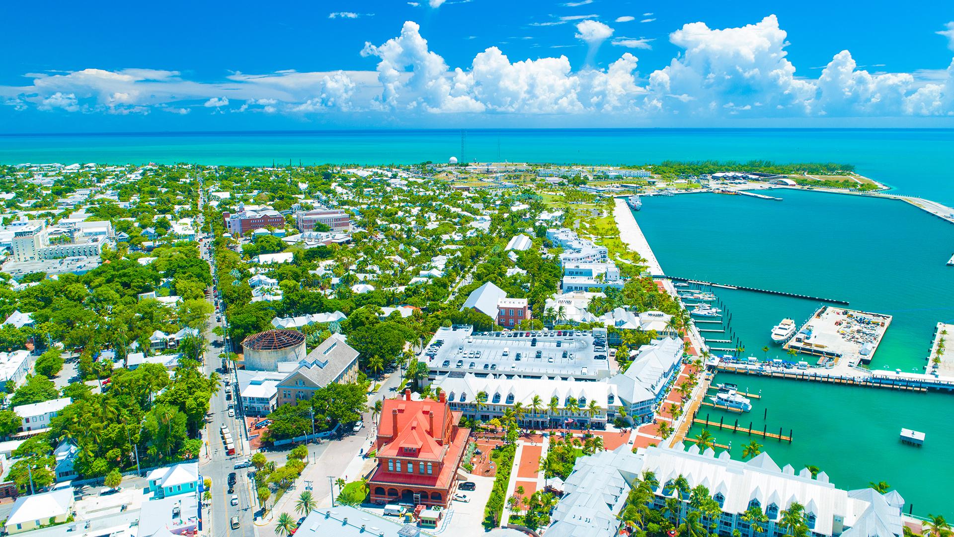 Vue aérienne de Key West en Floride avec maisons colorées, végétation tropicale et eau turquoise du port sous un ciel bleu.