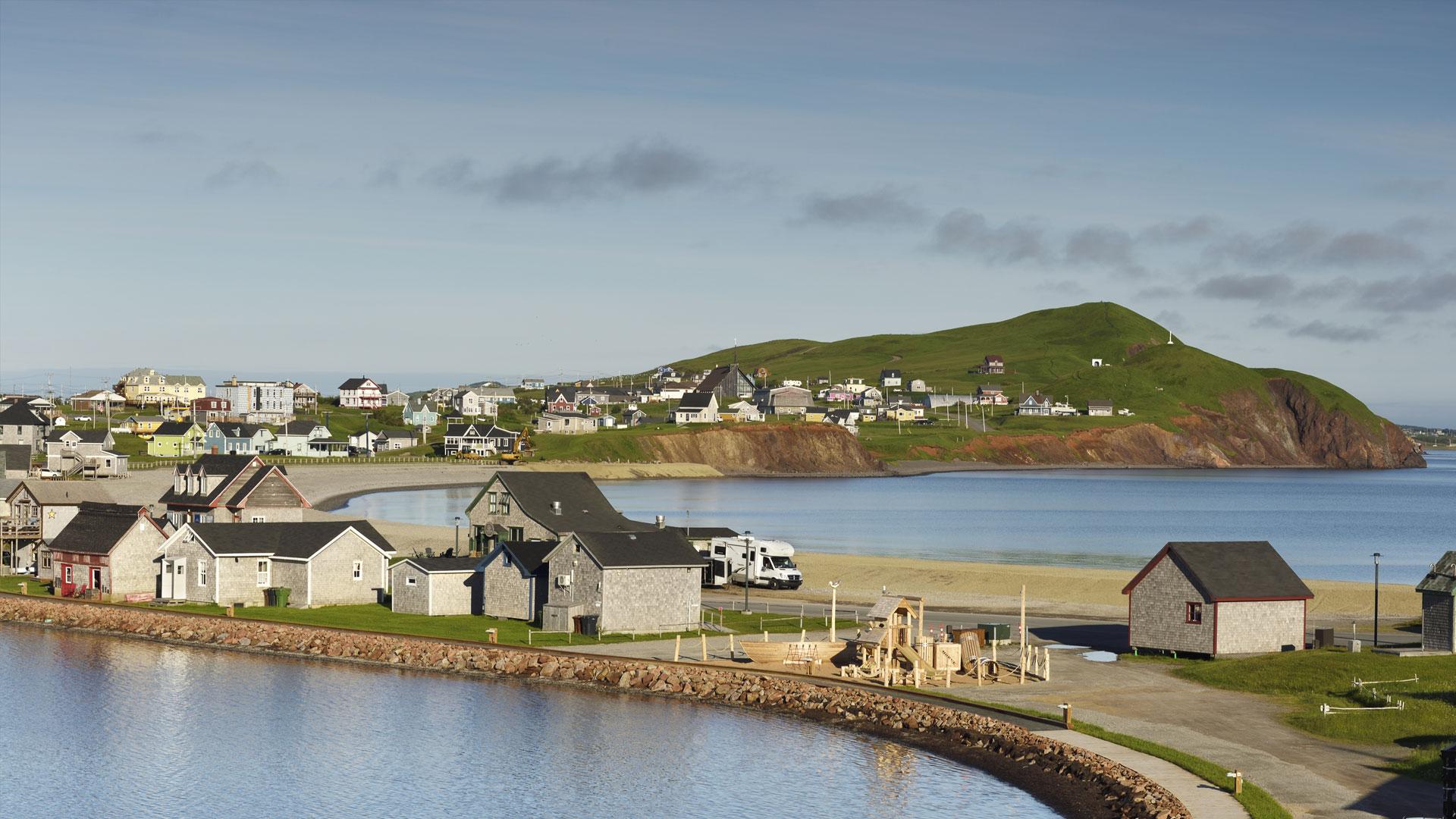 Maisons typiques de Havre-Aubert au bord de la mer avec plage, parc, quai et falaise rouge, aux îles de la Madeleine.