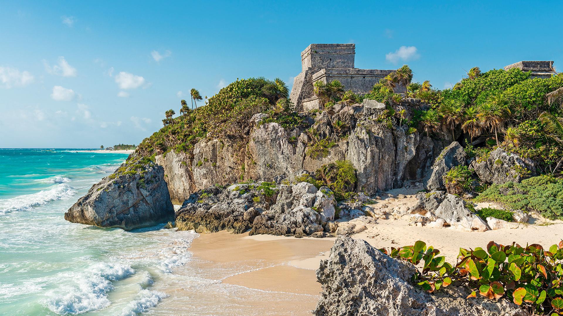 Ruines mayas de Tulúm perchées sur des rochers couverts de verdure, surplombant la mer turquoise et une plage de sable blanc.