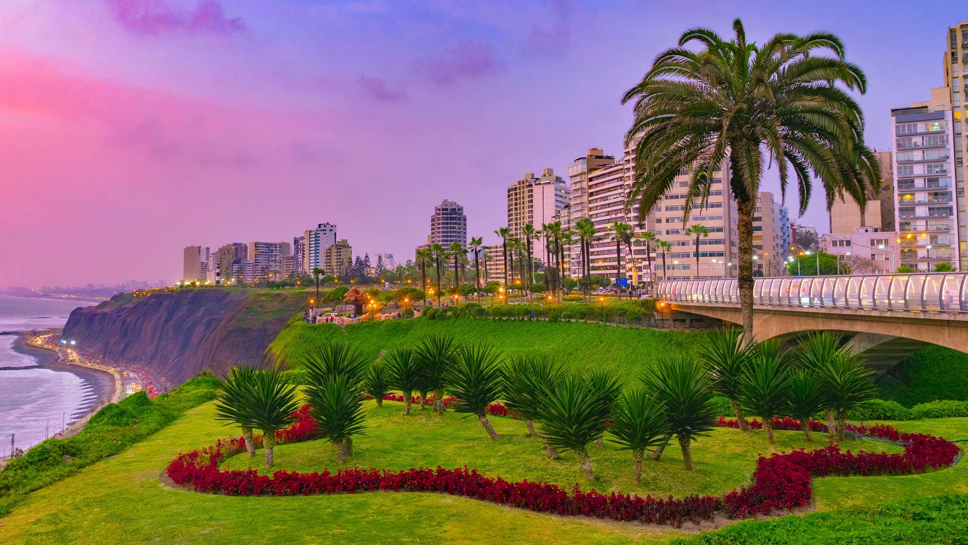 Vue panoramique de Lima, au Pérou, bordée par l’océan Pacifique avec édifices et palmiers sous un coucher de soleil violet.