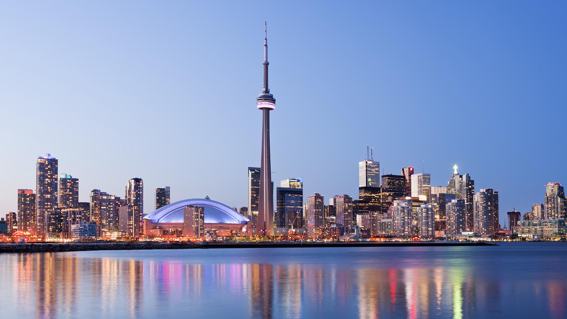 Vue de Toronto au crépuscule avec la Tour CN et le centre-ville illuminé se reflétant sur le lac Ontario, Canada.