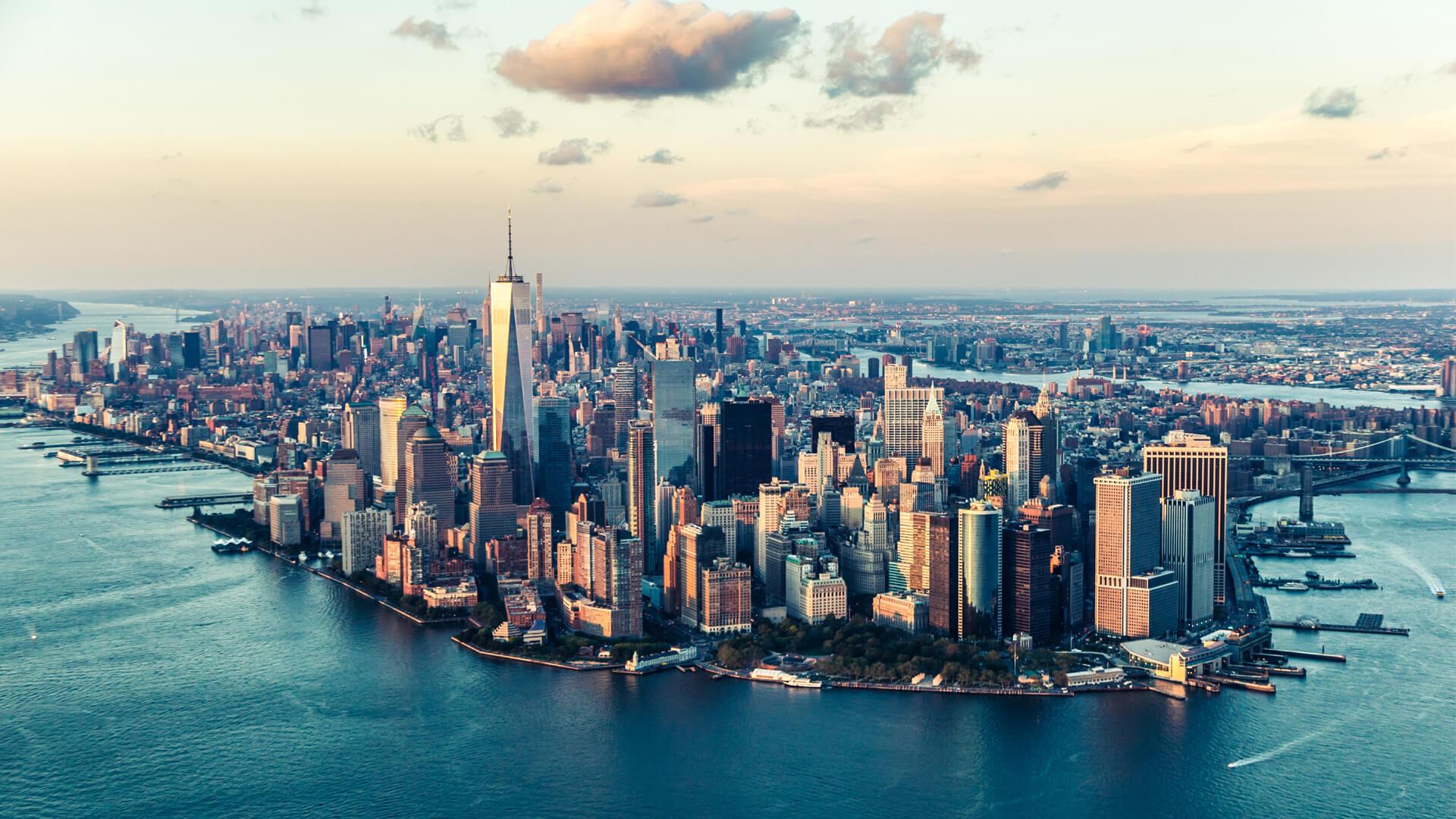 Vue aérienne de Manhattan, New York, avec le One World Trade Center dominant les gratte-ciel et la rivière bordant la ville.