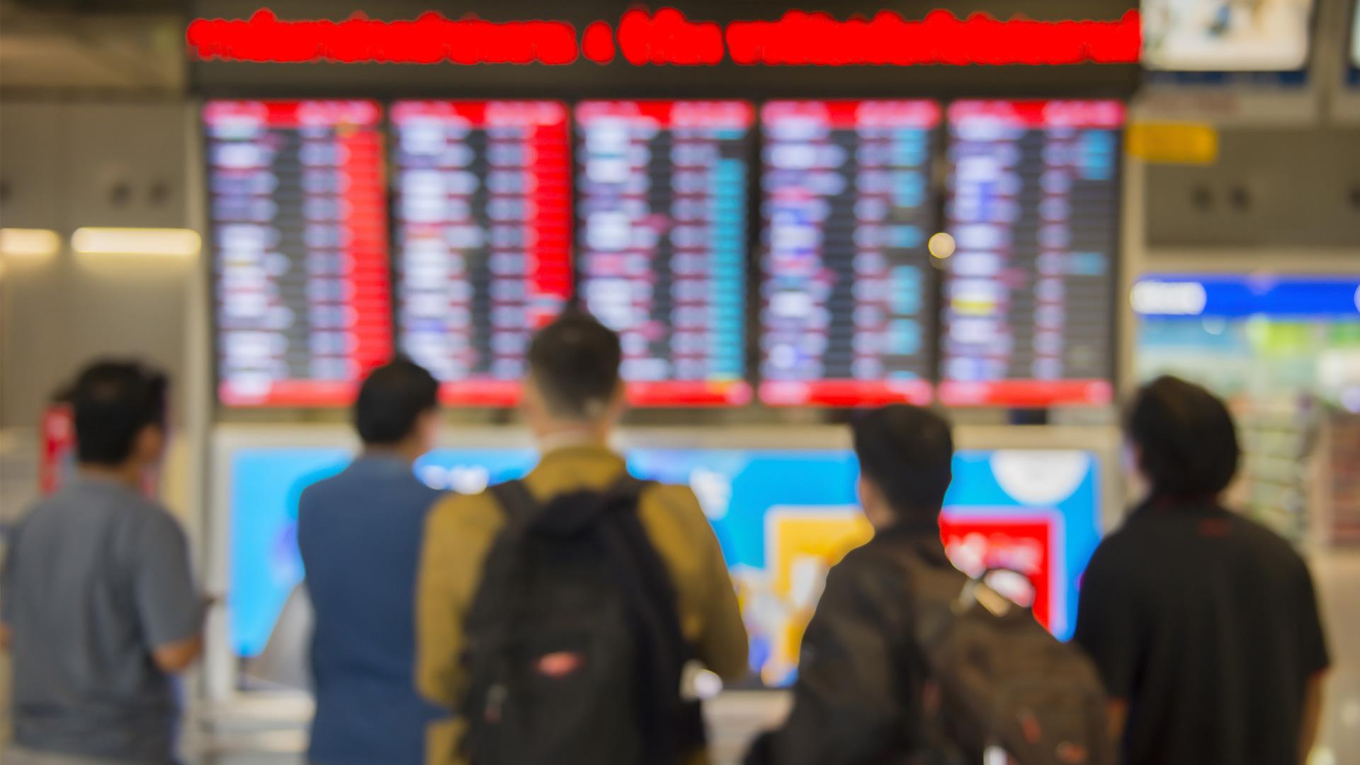 Dans un aéroport, des voyageurs regardent le panneau d’affichage des vols annulés.