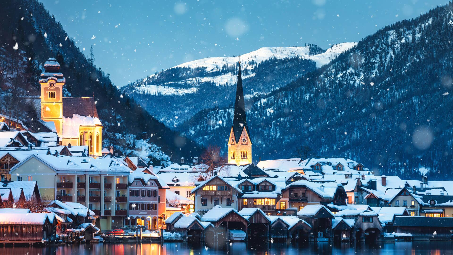 Village alpin de Hallstatt en hiver, au bord d’un lac en Autriche, avec les Alpes enneigées et des maisons illuminées.