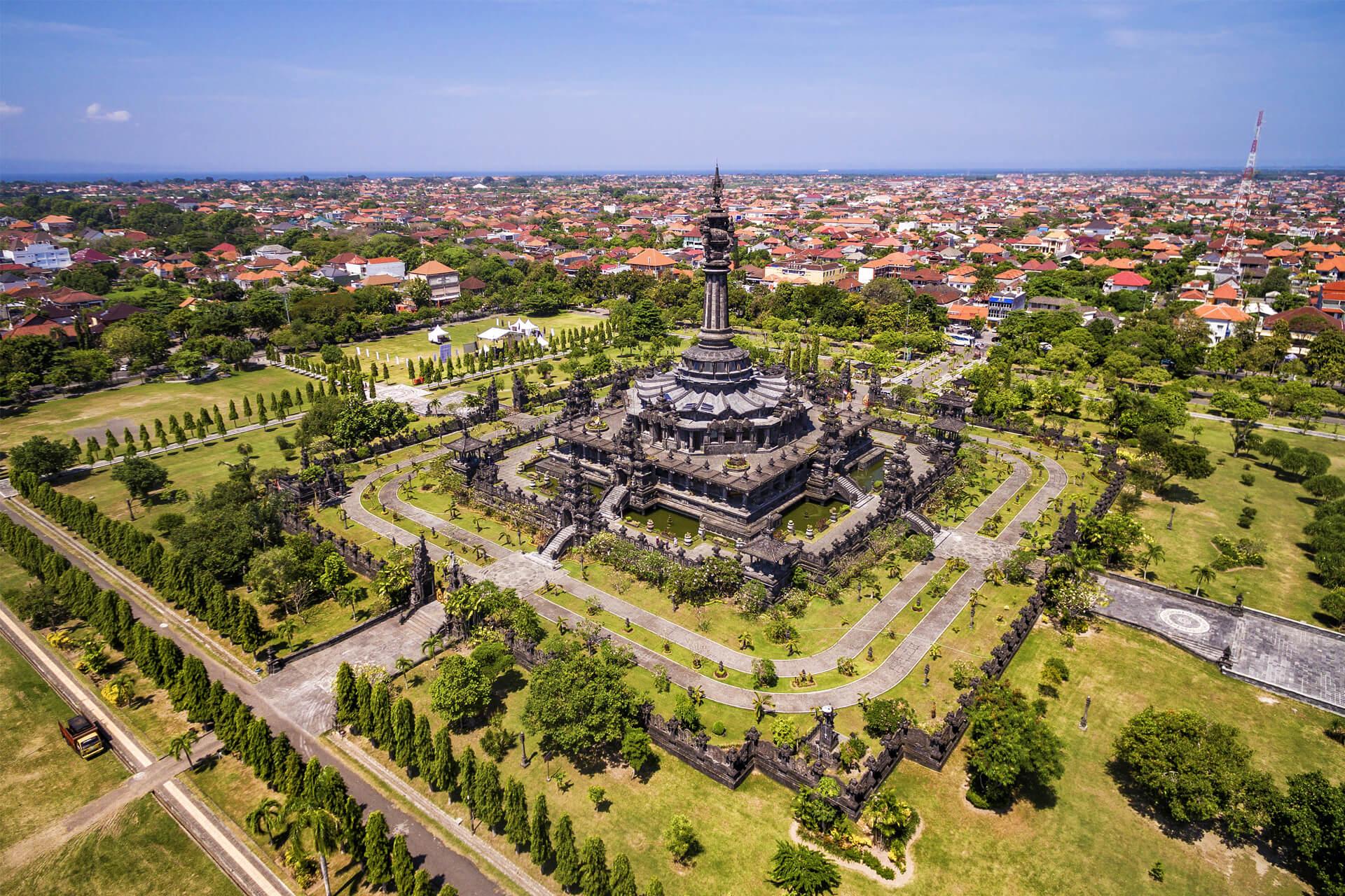 Vue aérienne du monument Bajra Sandhi à Denpasar, Bali, entouré d’un jardin verdoyant et d’allées d’arbres symétriques avec la ville en arrière-plan.