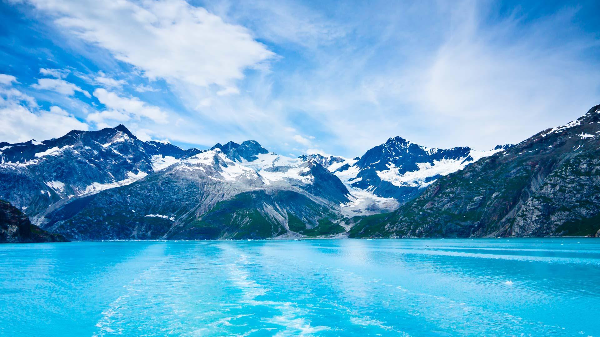 Glacier et eaux bleu clair au cœur d’un fjord d’Alaska, encadrés par des montagnes escarpées et enneigées.