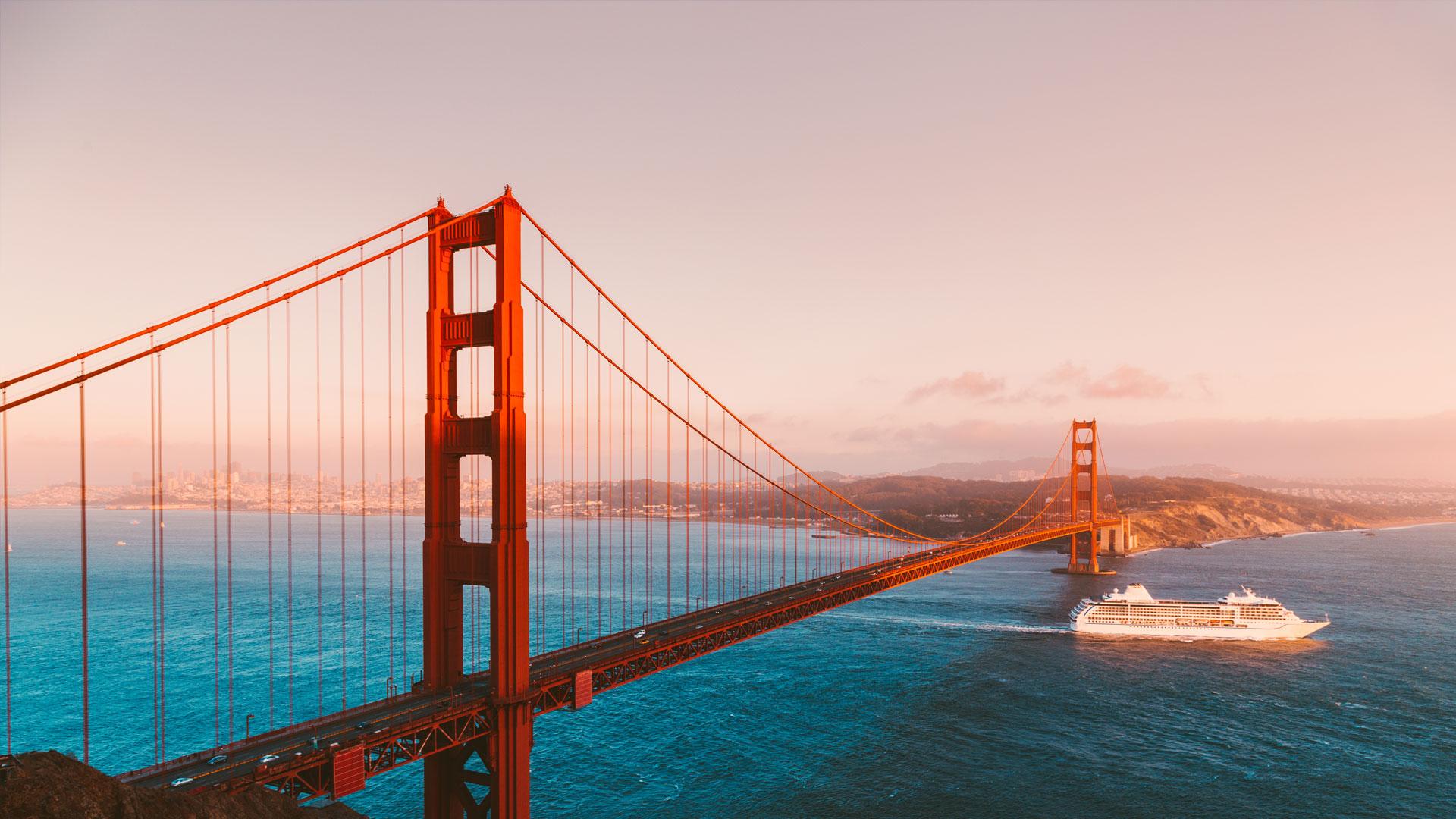 Golden Gate Bridge rouge orangé au coucher du soleil, contrastant avec les eaux turquoise de la baie de San Francisco.
