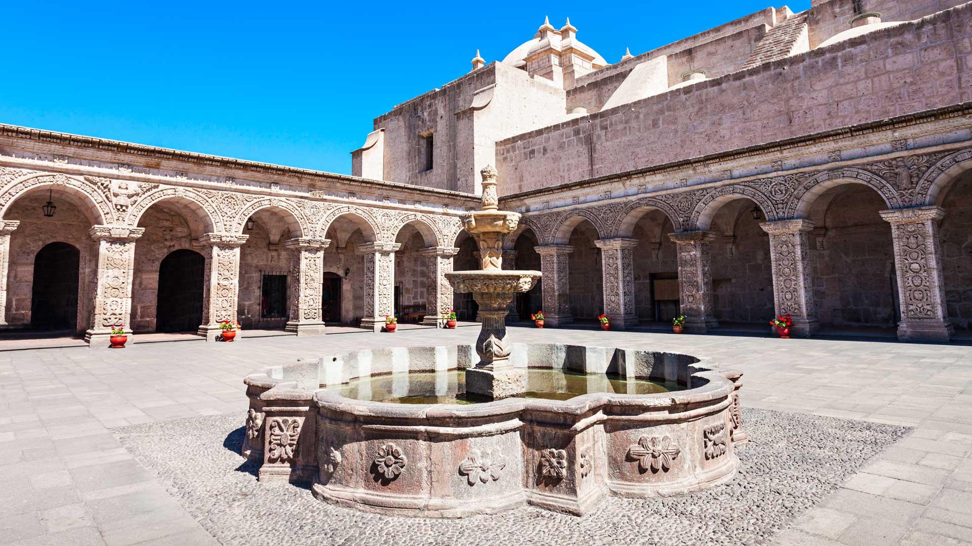 Cour intérieure de l’Iglesia de la Compania à Arequipa, au Pérou, ses cloîtres en sillar et sa fontaine centrale sous un ciel bleu.