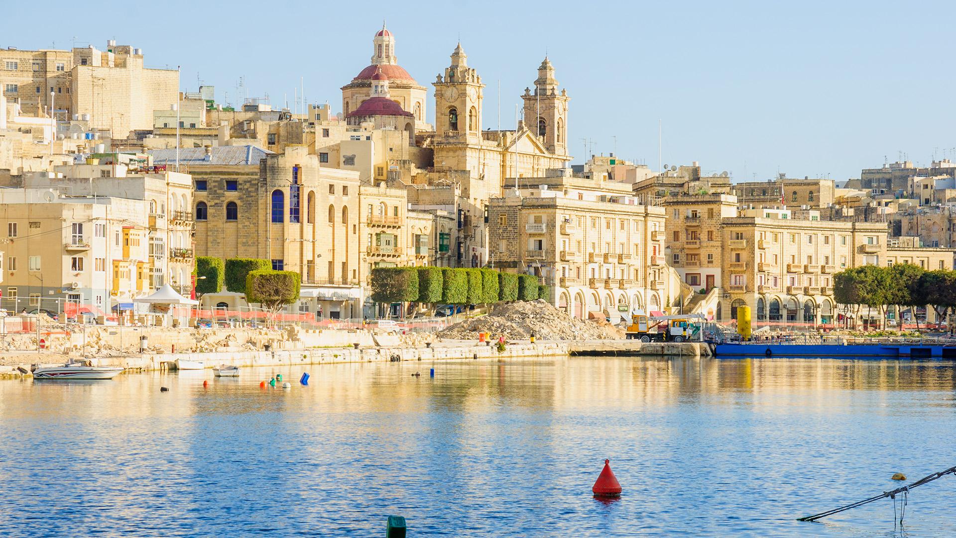 Vue sur Senglea, l’une des Trois Cités de Malte, avec façades couleur miel, clocher et eaux calmes du port au premier plan.