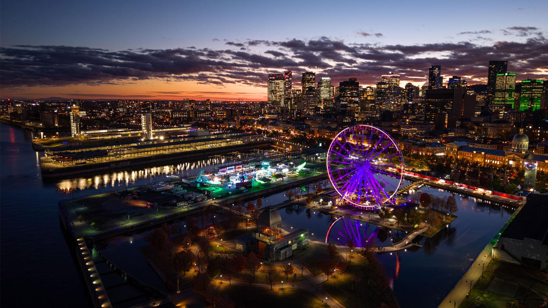 Montreal at sunset with its illuminated skyline, the Old Port observation wheel, and the St. Lawrence River.