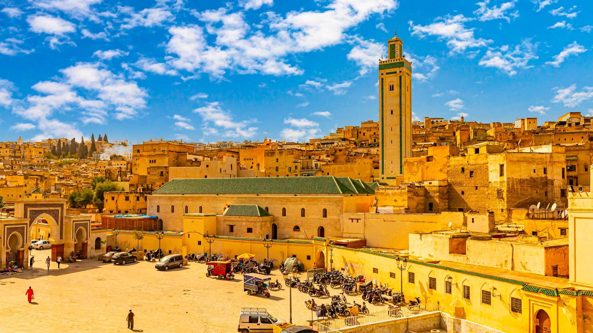 Vue panoramique de la médina de Fès au Maroc, avec ses bâtiments ocre, la mosquée et la porte Bab Bou Jeloud sous un ciel bleu.