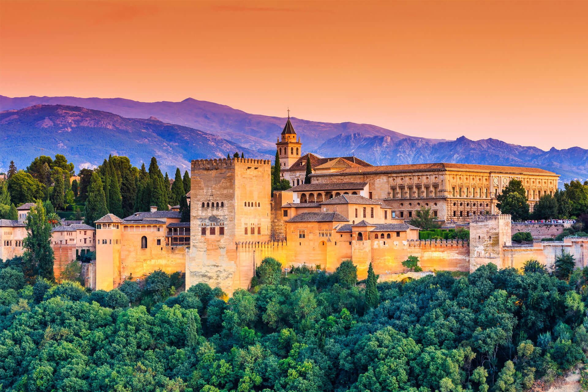 Vue de l’Alhambra à Grenade en Espagne, un palais fortifié entouré de forêts, avec montagnes en arrière-plan.