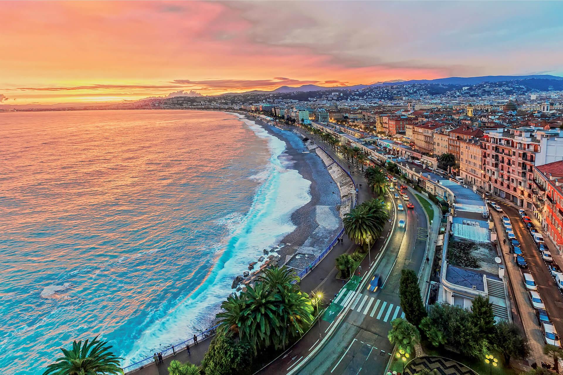 Bird’s-eye view of Nice’s Promenade des Anglais lined with palm trees along the Mediterranean Sea at sunset.
