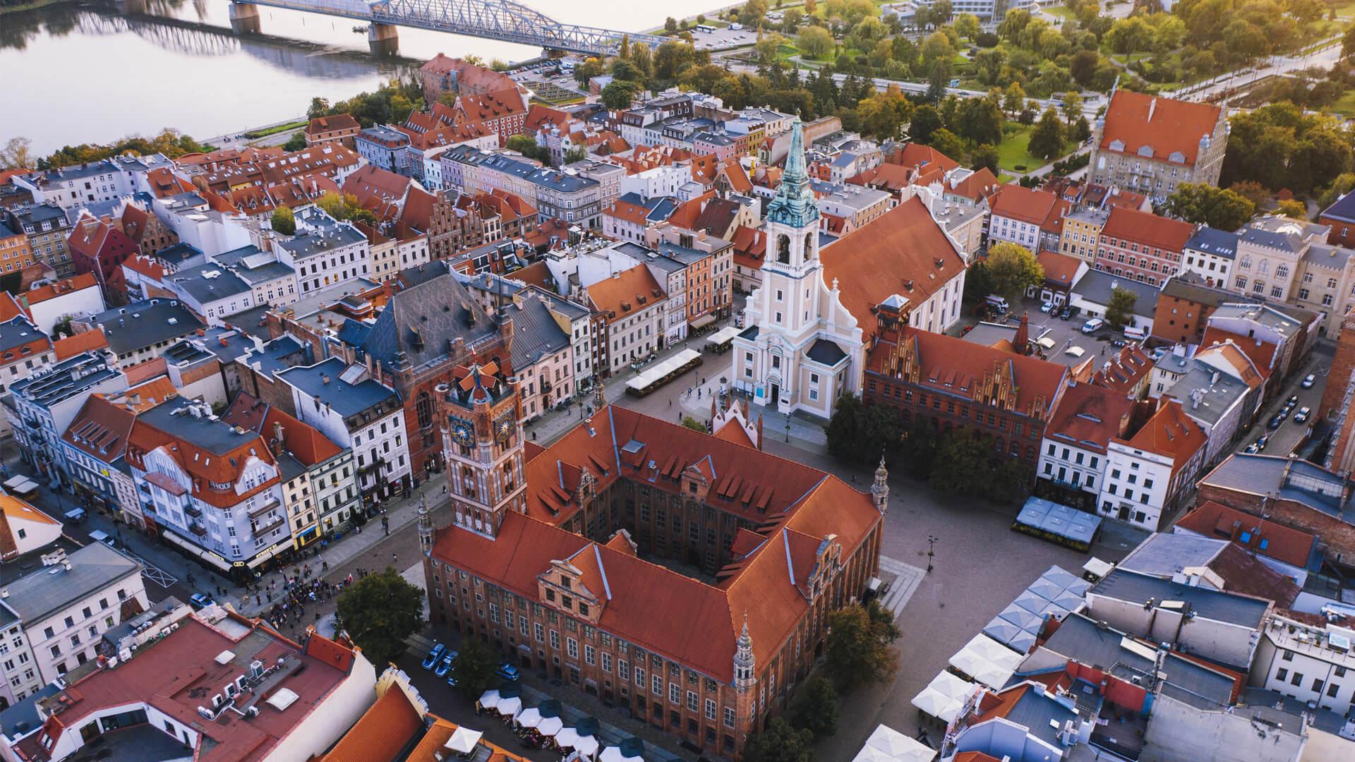 Aerial view of Toruń’s Old Town in Poland, with red rooftops and the Vistula River in the background.