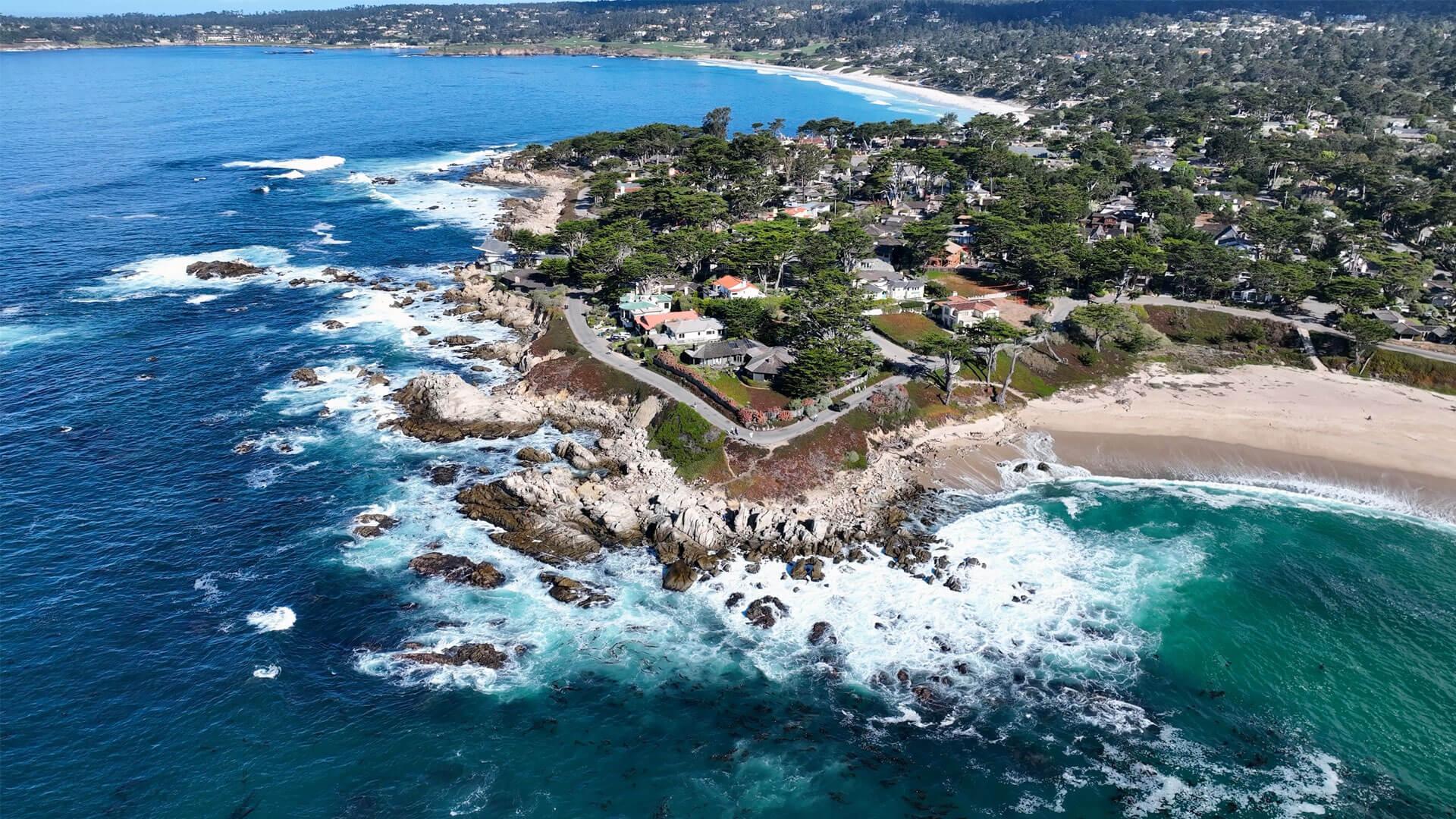 Vue aérienne de Carmel-by-the-Sea, avec ses falaises rocheuses, plages de sable clair, eaux turquoise et cyprès géants.