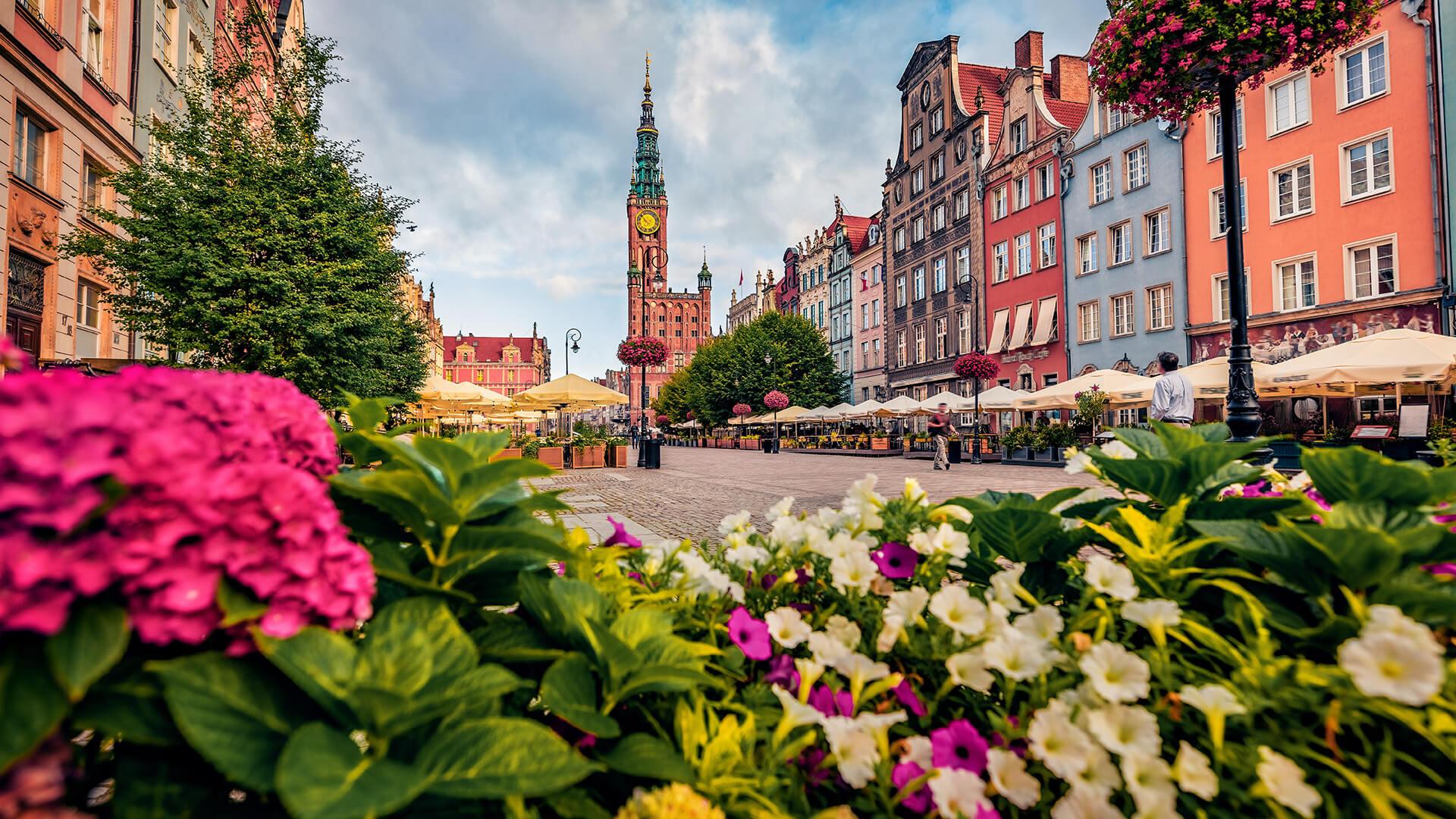 Long Market Square in Gdańsk, Poland, with colourful buildings, terraces, flowers, and the Town Hall in the background.