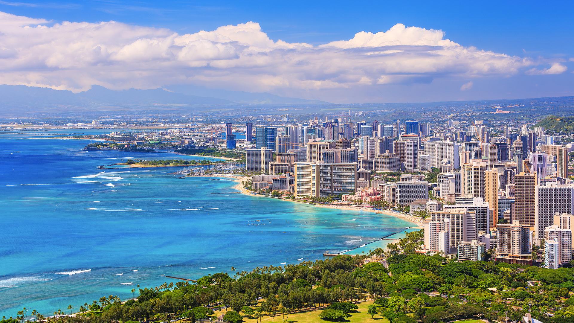 Aerial view of Honolulu, Hawaii’s capital, with lush green landscapes and buildings lining the coastline.
