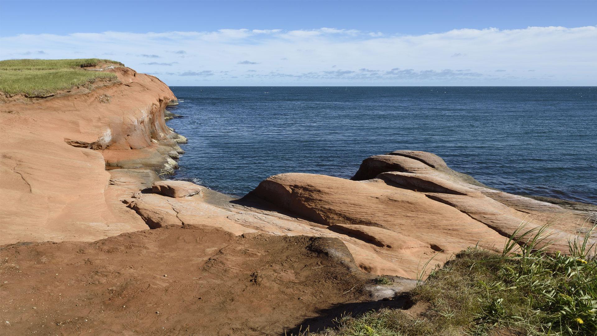 Falaises de grès rouge au bord du golfe du Saint-Laurent avec végétation et ciel bleu aux îles de la Madeleine.