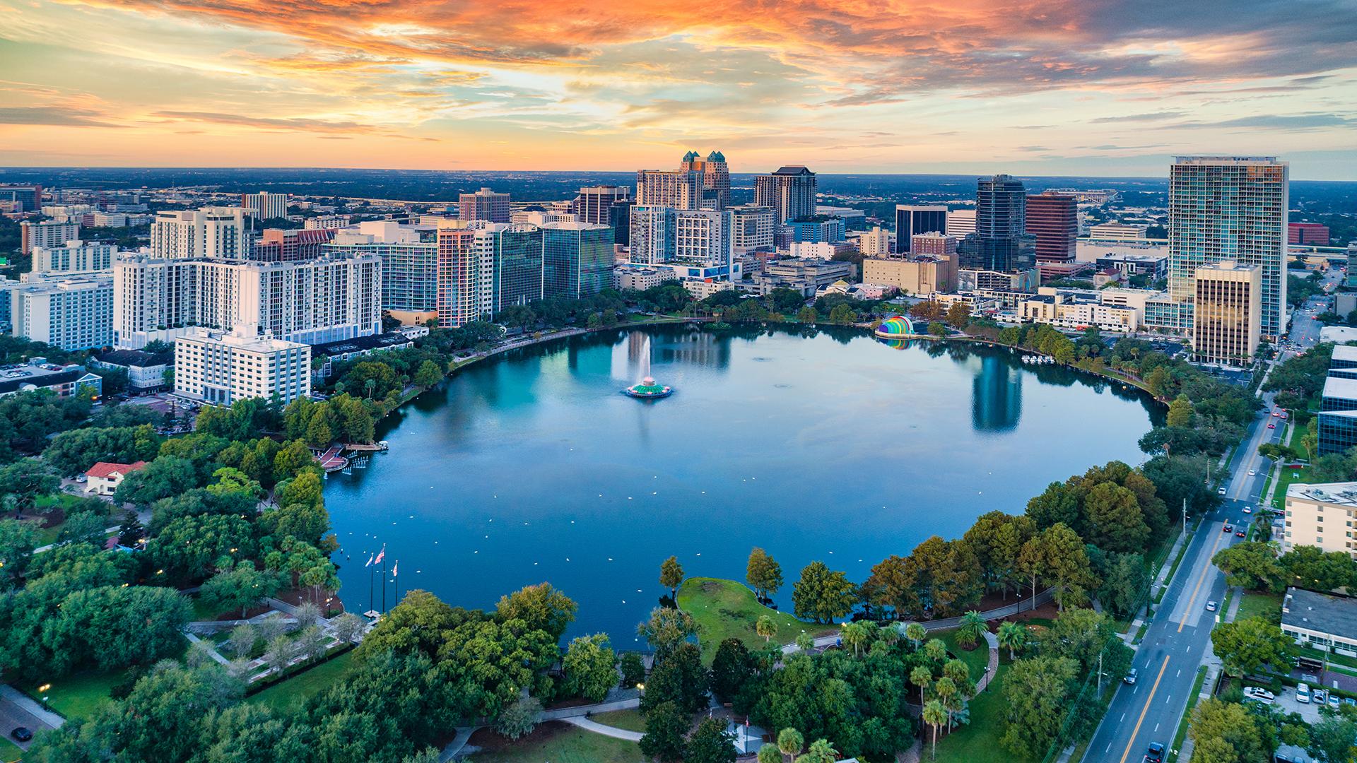 Vue aérienne d’Orlando en Floride avec Lake Eola Park au centre, entouré de gratte-ciels et d’espaces verts au coucher du soleil.