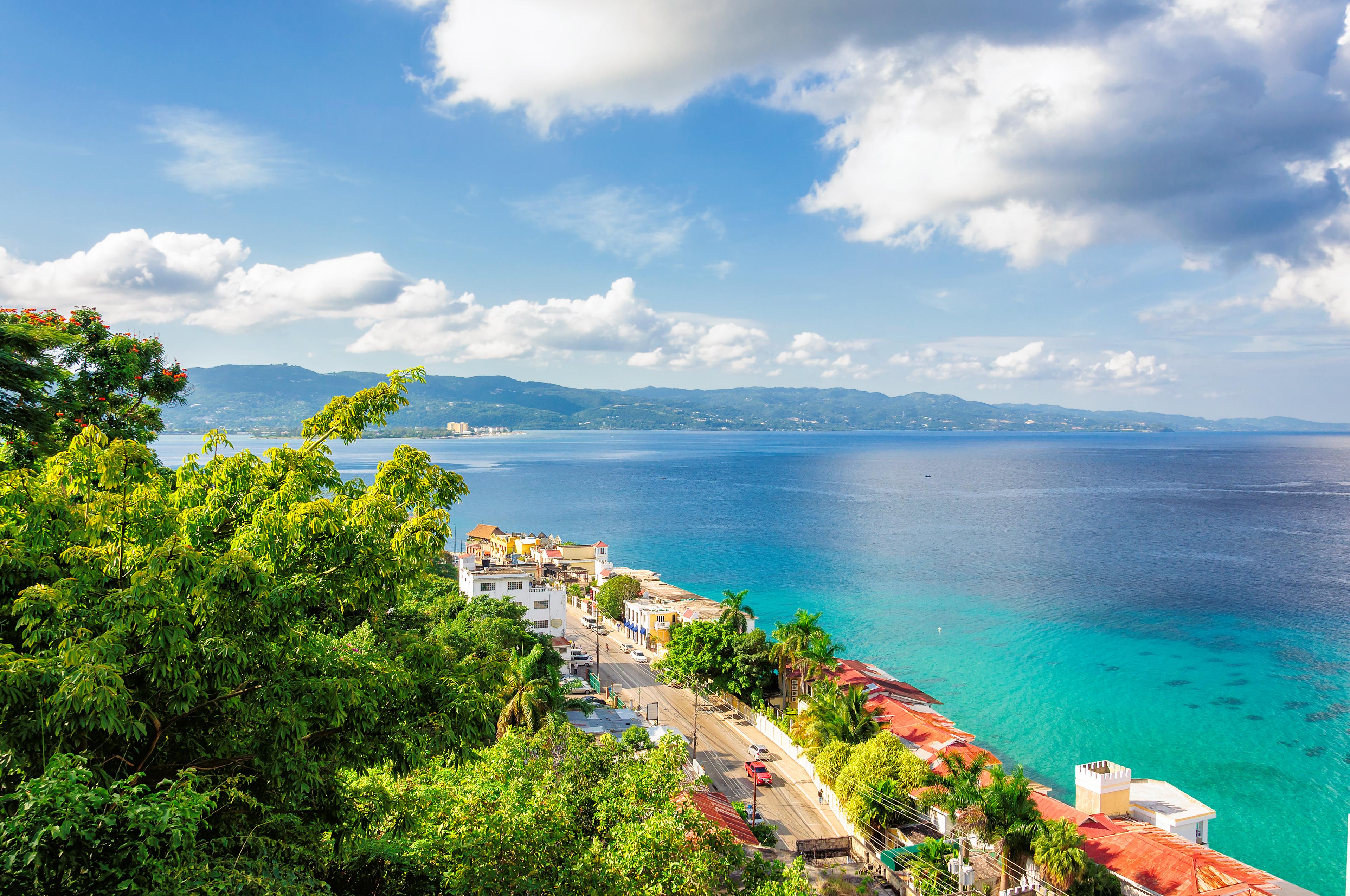 Panoramic view of a rocky Montego Bay beach in Jamaica at sunset, with clear waters and a lone palm tree.