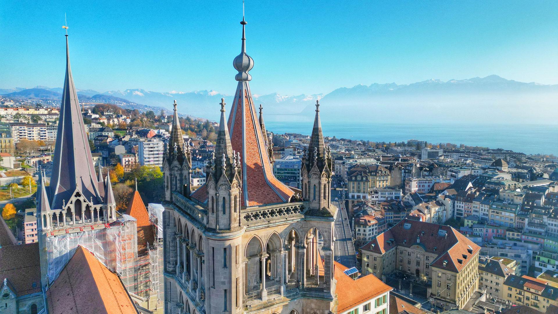 Aerial view of Lausanne, Switzerland, featuring the Notre-Dame Cathedral with its stone roof and prominent spire.