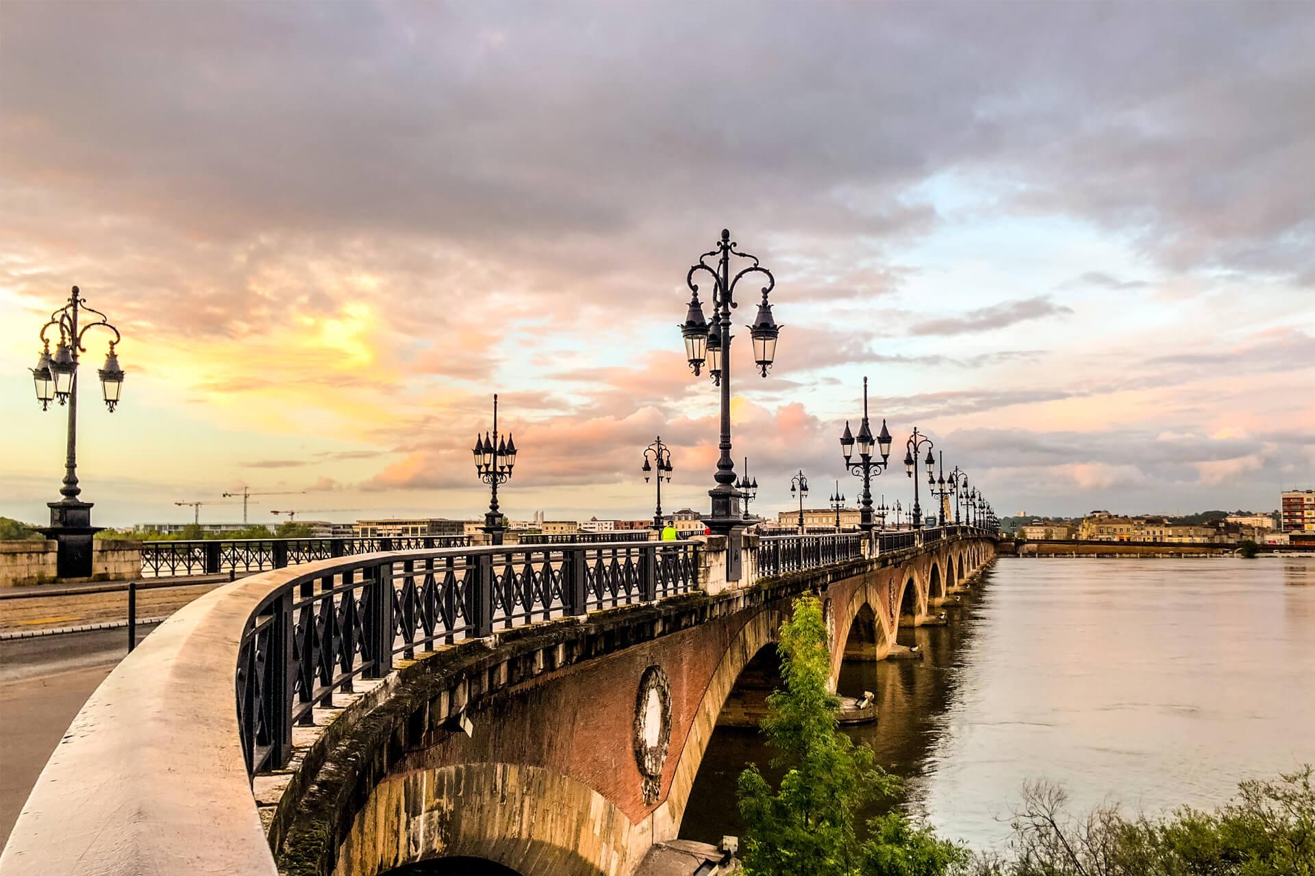 The Pont de Pierre in Bordeaux, France, with its elegant arches and Haussmann lampposts spanning the Garonne River at sunset.