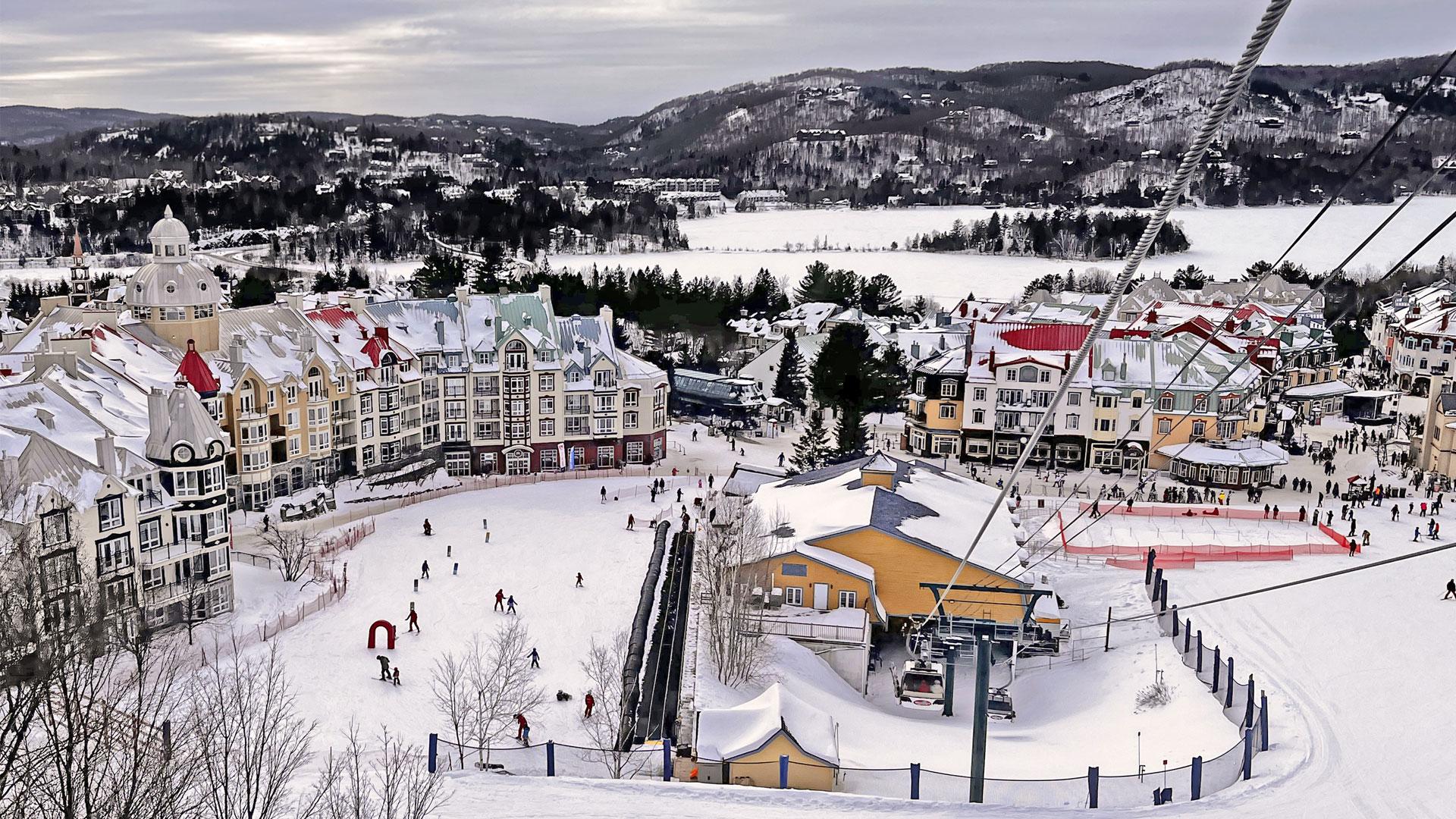 Colourful village of Mont-Tremblant under snow, with skiers, ski lifts, and the hills of the Laurentians.