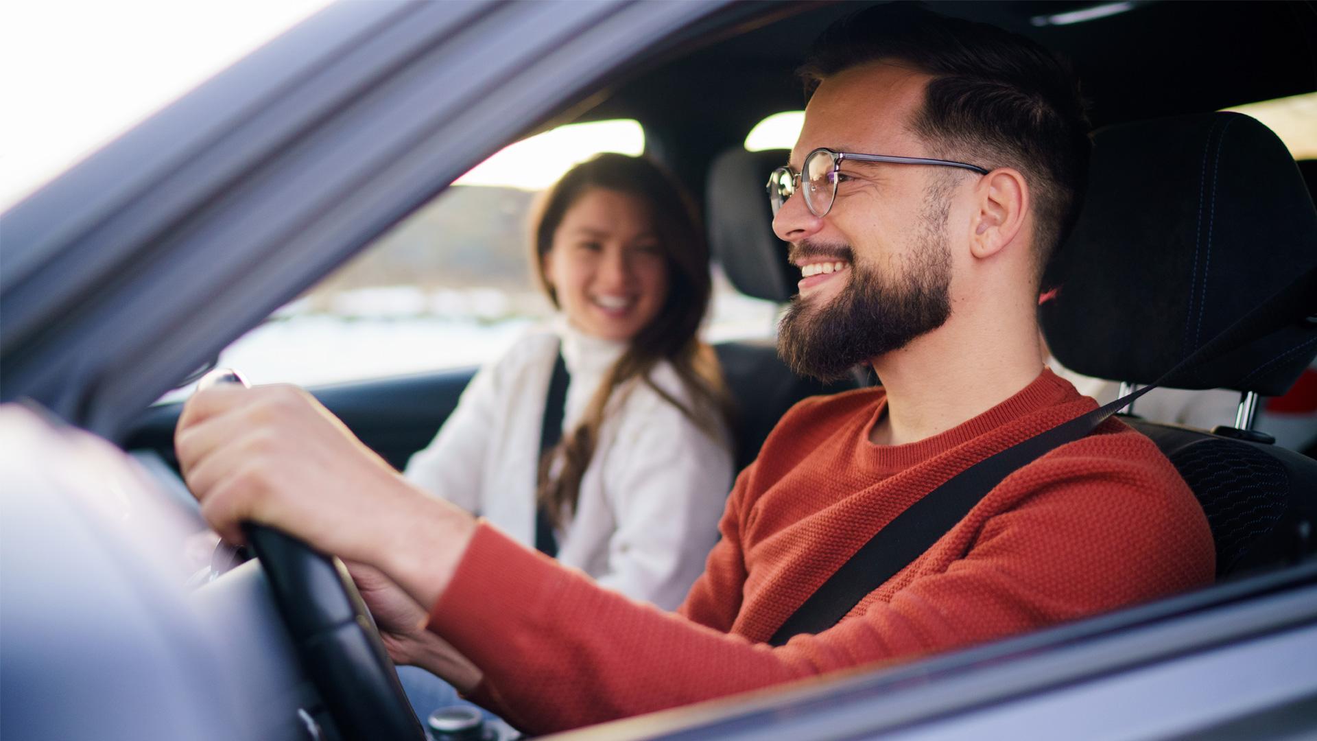 Un homme tout sourire est très fier de conduire sa nouvelle voiture d’occasion.