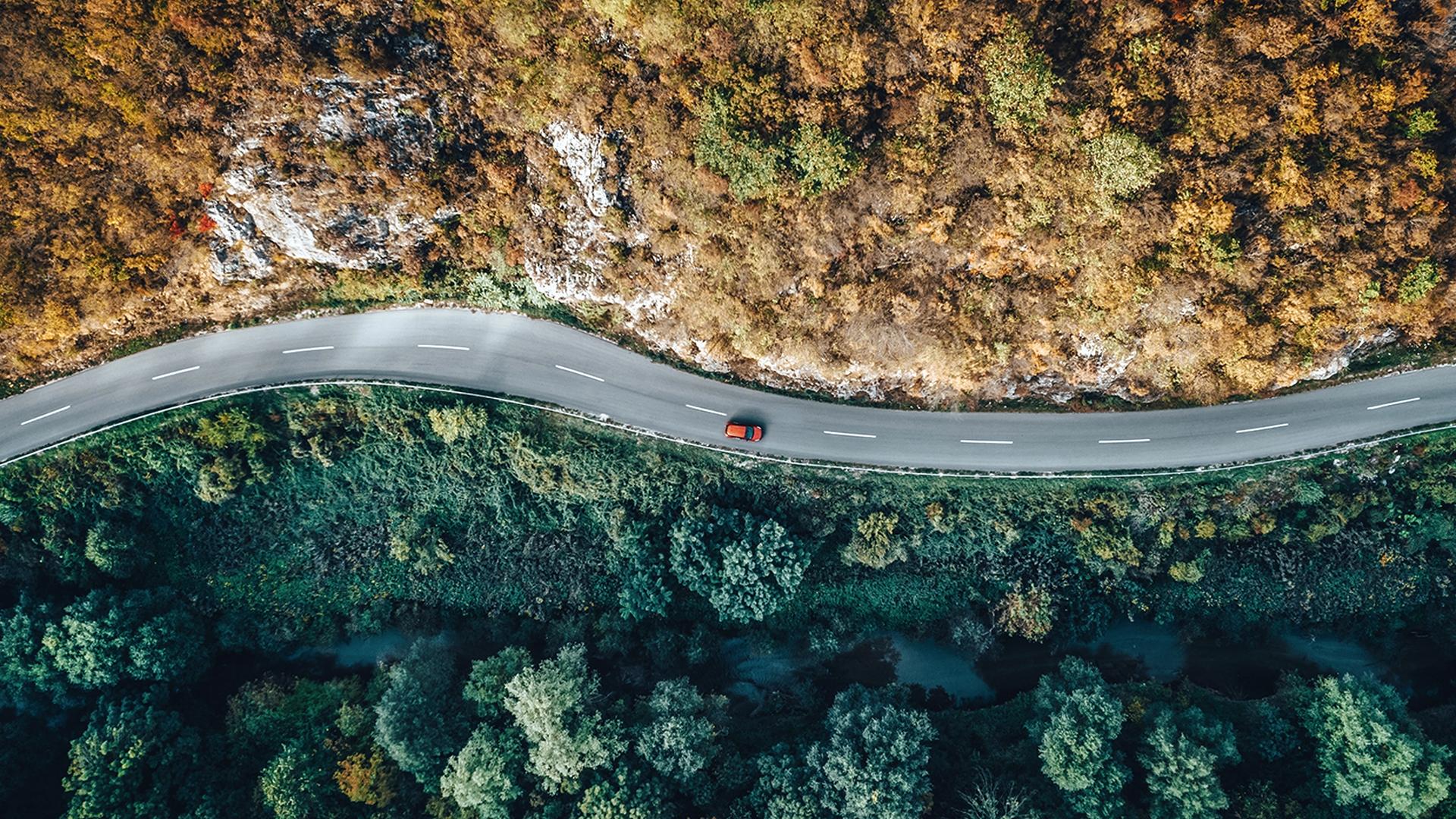 Une voiture roule sur une route sinueuse, entre montagne et forêt.