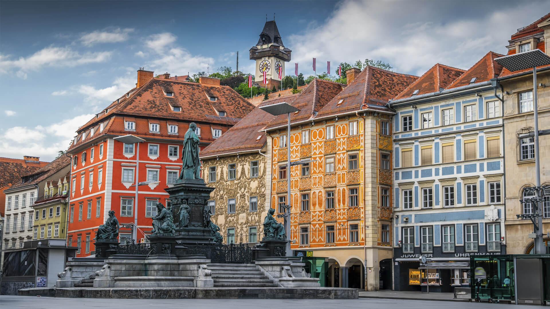 Hauptplatz, the central square of Graz, Austria, with colourful historic buildings, a fountain and the Clock Tower in the background.