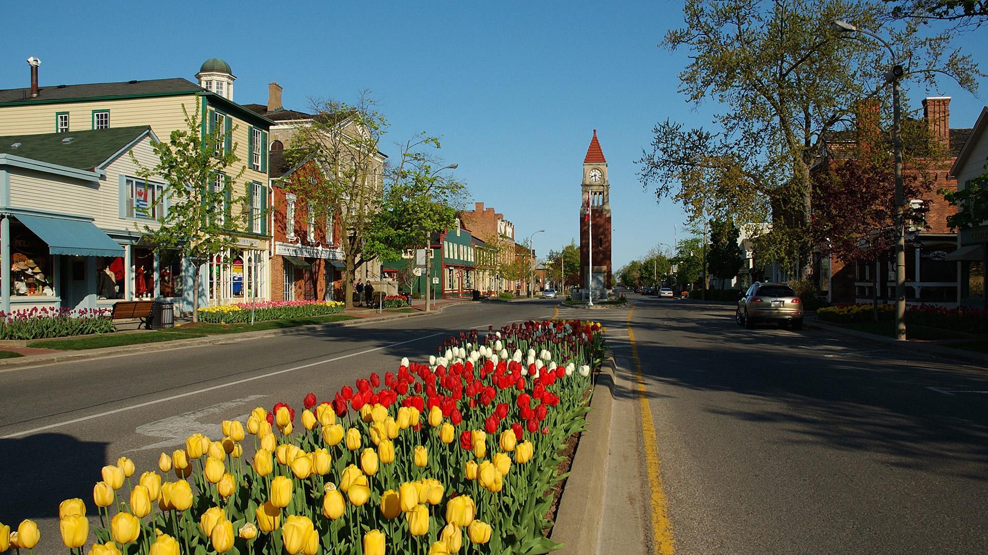 Rue Queen Street à Niagara-on-the-Lake, bordée de maisons historiques colorées et de tulipes, avec la tour de l’horloge au loin.
