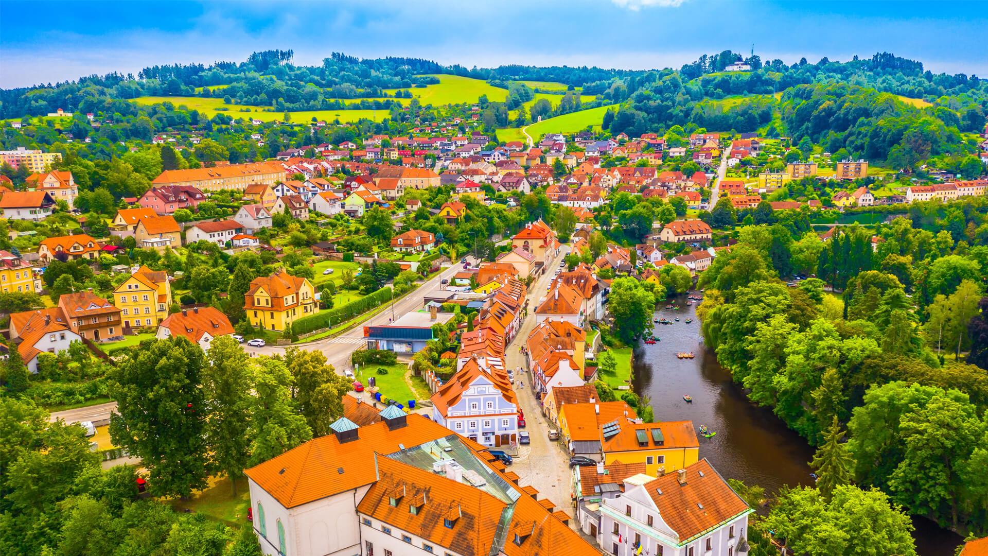 Vue aérienne de Český Krumlov en Tchéquie, ses maisons aux toits orange, une rivière et des collines verdoyantes.