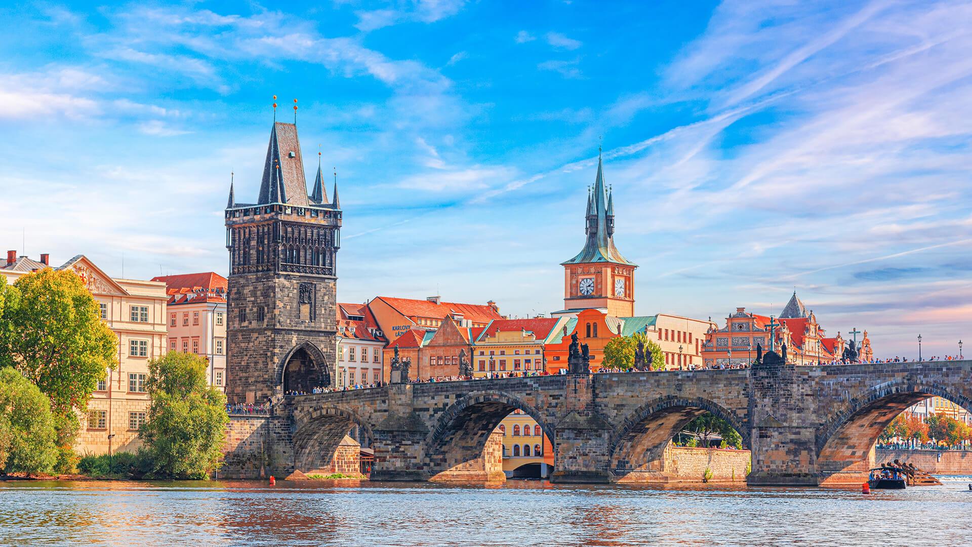Panoramic view of Charles Bridge in Prague, the Vltava River, and the historic buildings of the Old Town in the background.